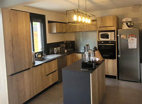 Cuisine aménagée en U type ambiance industrielle, design et etndance, avec des façades en chê,n cognac et un plan de travail soft touch en coloris noir