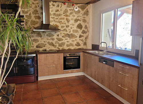 Cuisine traditionnel en L dans un bel environnement avec un mur en pierre, façades chêne brut et plan de travail en gris anthracite